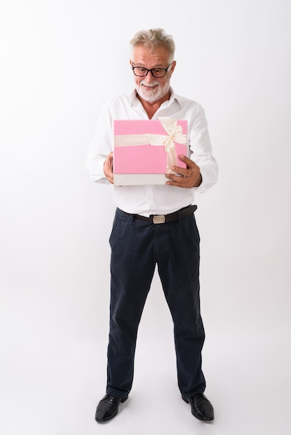 Foto de corpo inteiro de um homem barbudo sênior feliz sorrindo e em pé ao abrir uma caixa de presente em branco