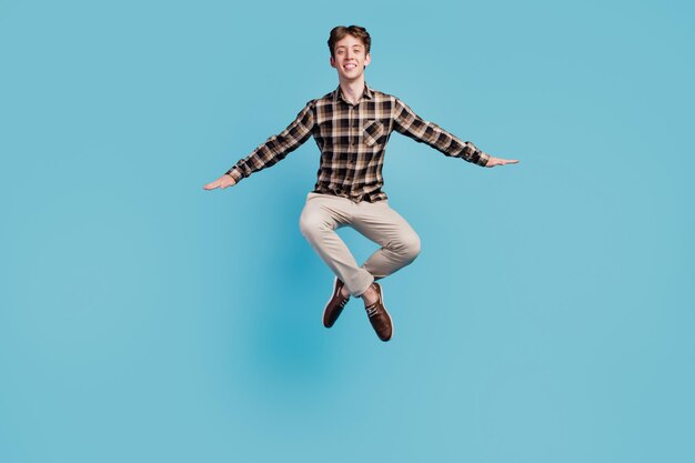 Foto de corpo inteiro de um jovem alegre e animado se divertindo, salto ativo isolado sobre fundo de cor azul