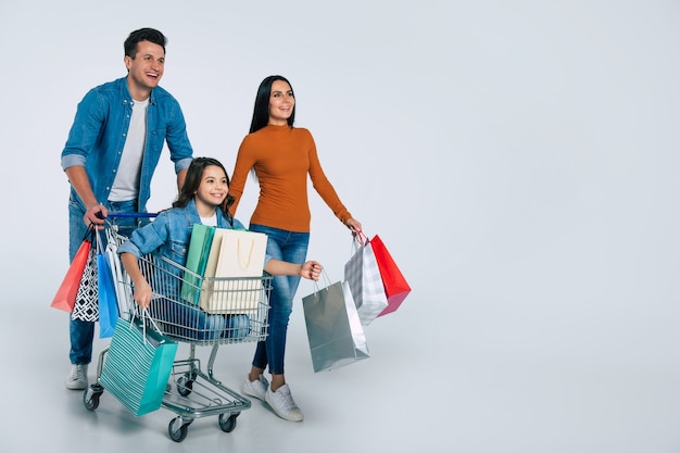 Foto de corpo inteiro de uma família nas compras, se abraçando, olhando para a câmera com grandes sorrisos e segurando suas novas compras nos braços.