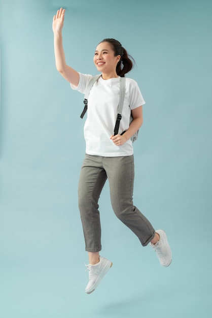 Foto de corpo inteiro de uma garota alegre segurando mochila, salto, corrida, lição, cumprimenta os colegas de classe sobre fundo azul