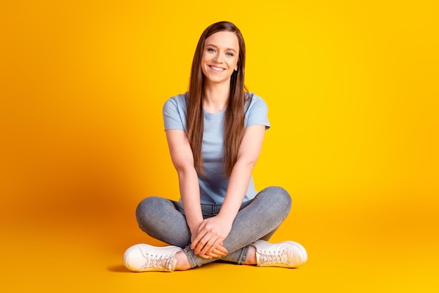 Foto foto de corpo inteiro de uma jovem encantadora, de bom humor, sente-se no chão, aproveite o tempo livre isolado sobre o fundo amarelo