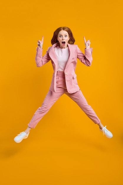 Foto de corpo inteiro de uma senhora caucasiana engraçada em um terno rosa pulando alto, veja os preços baixos de compra, direcione o dedo para cima no banner de anúncio isolado fundo de cor amarela no estúdio