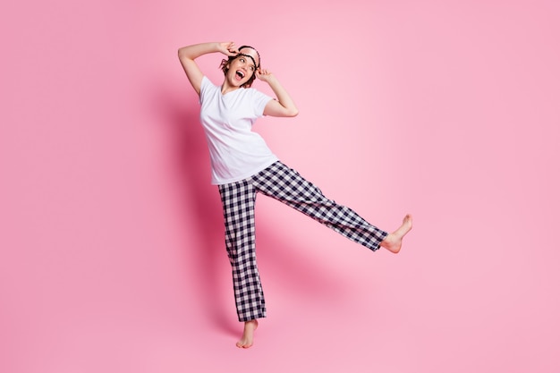 Foto de corpo inteiro de uma senhora engraçada levantando a perna se divertindo de pijama na parede rosa