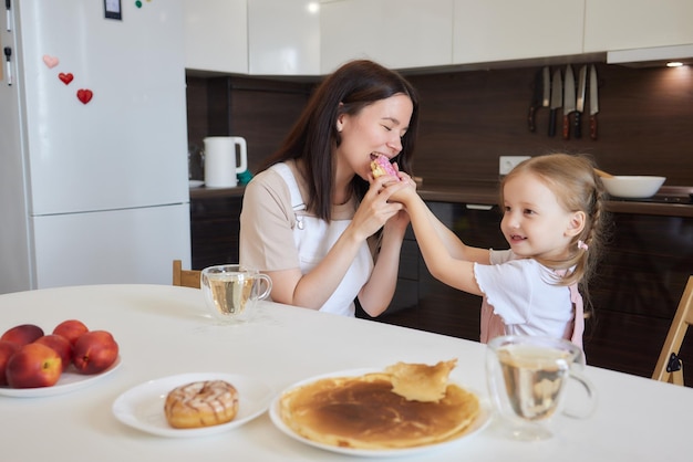 Foto de corte da mãe de vermelho e sua filha com donuts coloridos sentados na cozinha Conceito de dieta e junk food