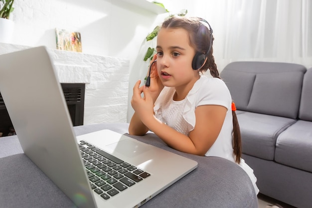 Foto de criança positiva menina estudo remoto sentar mesa mesa usando laptop tem aula de comunicação online com tutor redigindo relatório em casa dentro de casa