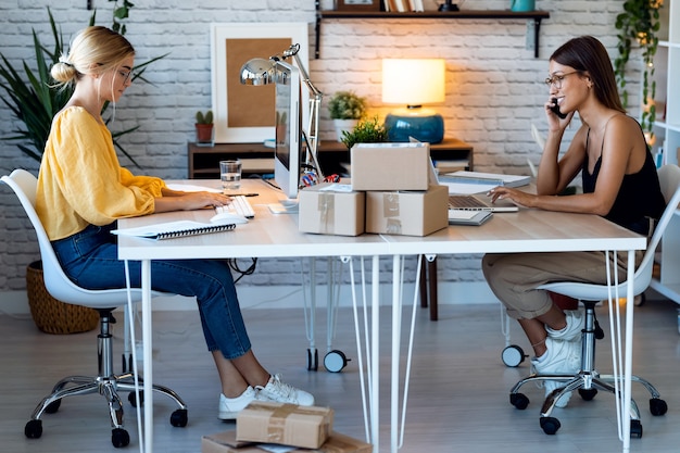 Foto de duas belas vendedor de mulheres de negócios freelance trabalhando com o computador enquanto falava com o telefone inteligente em sua pequena empresa de inicialização.