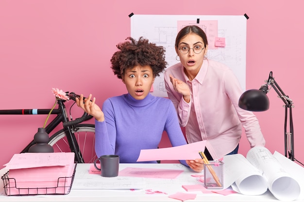 Foto de duas colegas de trabalho perplexas olhando indignadas, percebendo que os mortos não têm muito tempo para terminar a pose de trabalho do projeto no espaço de coworking