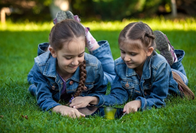 Foto de duas irmãs pequenas com um tablet deitada na grama no parque
