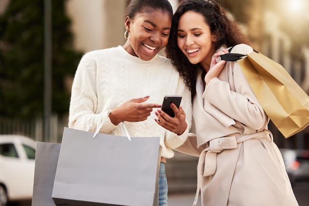 Foto de duas jovens usando um smartphone enquanto fazia compras em um ambiente urbano