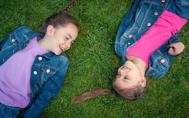 Foto de duas meninas deitadas na grama, cara a cara, rindo