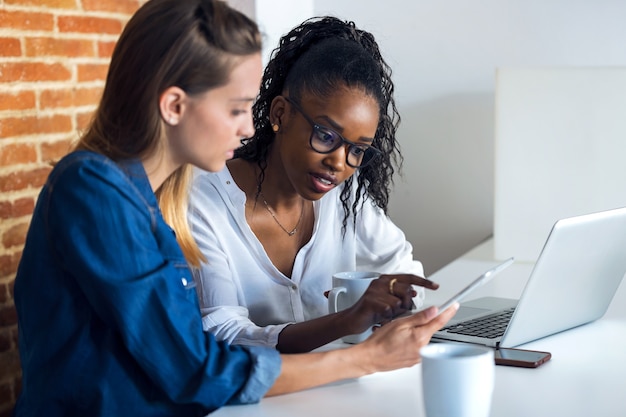 Foto de duas mulheres de negócios muito jovens trabalhando em conjunto com o tablet digital no escritório.