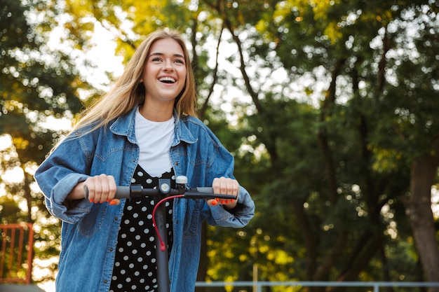 Foto de emocional satisfeito feliz jovem adolescente do lado de fora no parque verde natureza andando com scooter.