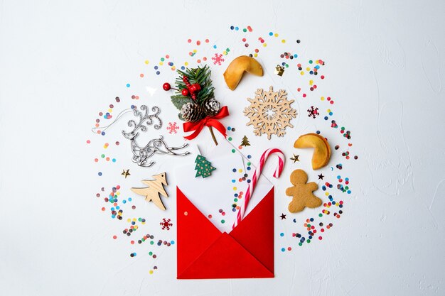 Foto de envelope vermelho, biscoitos e decoração de Natal em uma superfície branca vazia