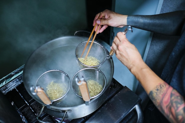 Foto de estoque de chef não reconhecido cozinhando macarrão na cozinha de um restaurante japonês.