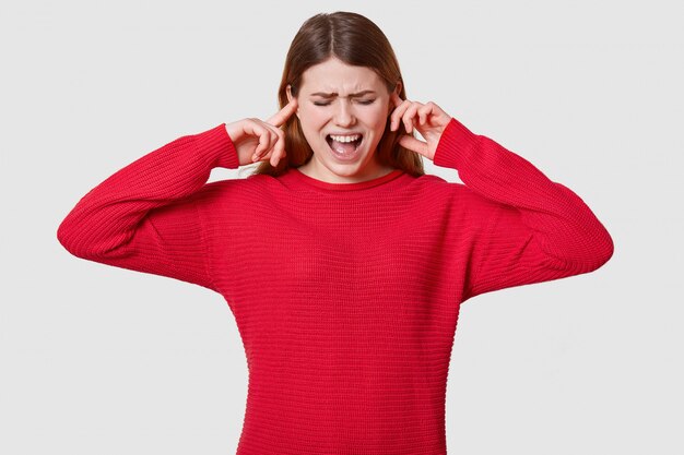 Foto de estressante mulher de cabelos escuros, vestindo jumper vermelho, entrando em pânico, não quer ouvir nada, se sente desesperada