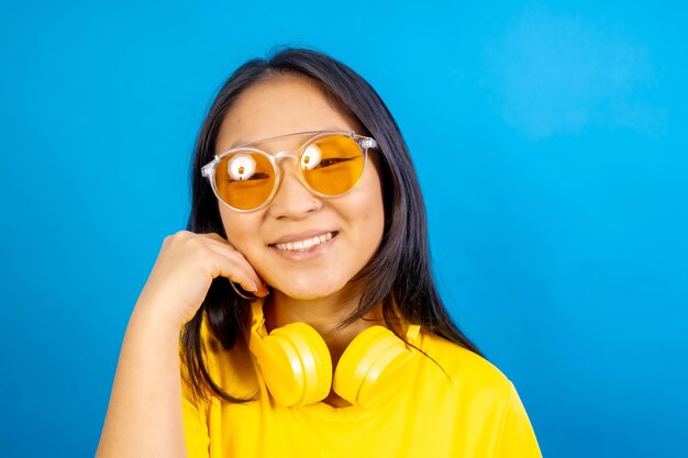 Foto foto de estúdio com fundo azul de uma mulher chinesa tímida e bonita usando óculos de sol sorrindo para a câmera