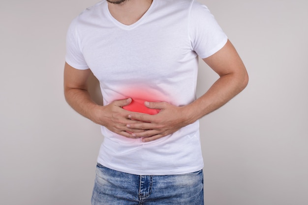 Foto de estúdio cortada close-up retrato de chateado triste com medo preocupado com intestino perturbado tendo distúrbio de dor de estômago usar calças jeans isoladas de fundo cinza