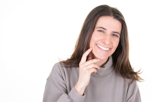 Foto de estúdio da modelo de uma bela jovem olhando para a câmera com um sorriso fofo e encantador enquanto posa contra a parede do espaço branco da cópia