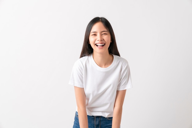Foto de estúdio de alegre linda mulher asiática em camiseta branca e ficar na parede branca.