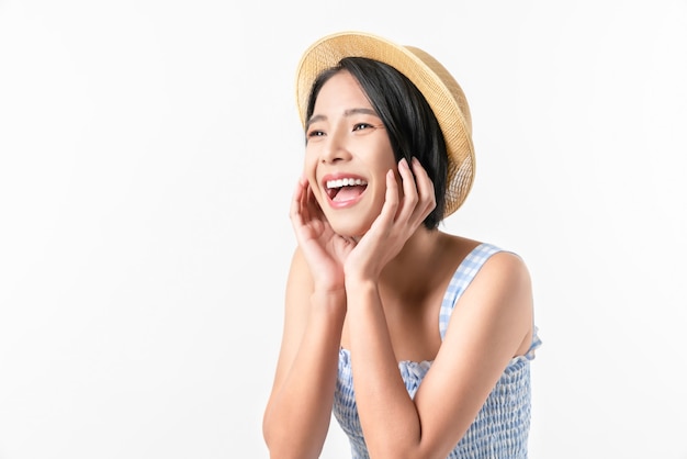 Foto de estúdio de alegre linda mulher asiática no vestido de cor azul e usando um chapéu e um pé no fundo branco.