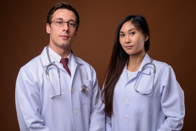 Foto de estúdio de dois jovens médicos juntos contra um fundo marrom