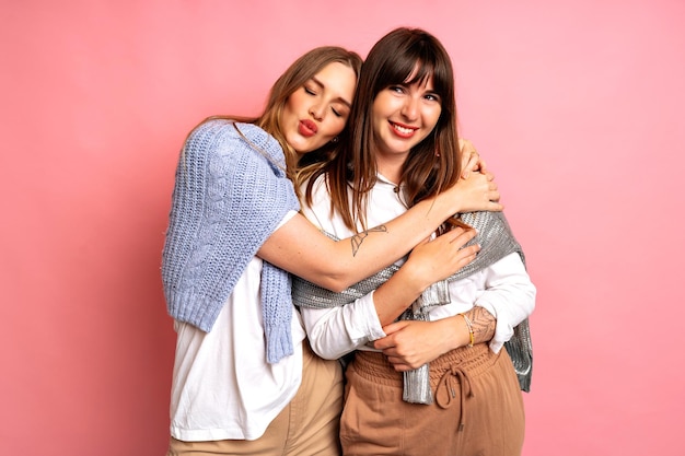 Foto foto de estúdio de duas mulheres bonitas em camisolas aconchegantes, posando sobre fundo rosa. tendências da moda outono e inverno. emoções positivas e abraços.