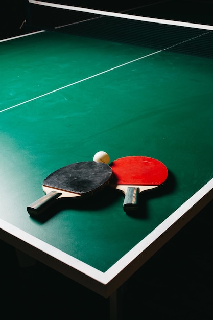 Foto de estúdio de duas raquetes de pingue-pongue e uma bola estão na mesa de jogo verde