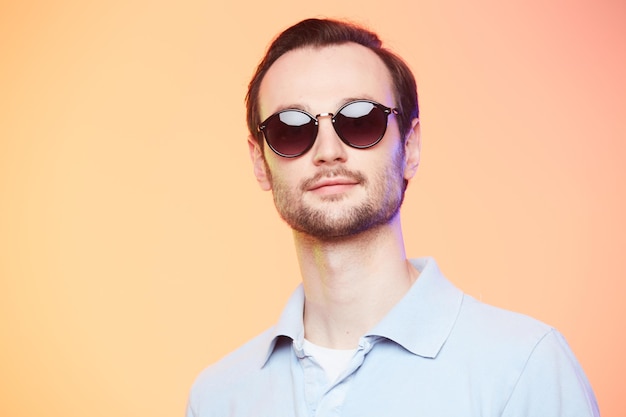 Foto de estúdio de homem bonito usando óculos escuros sobre fundo laranja