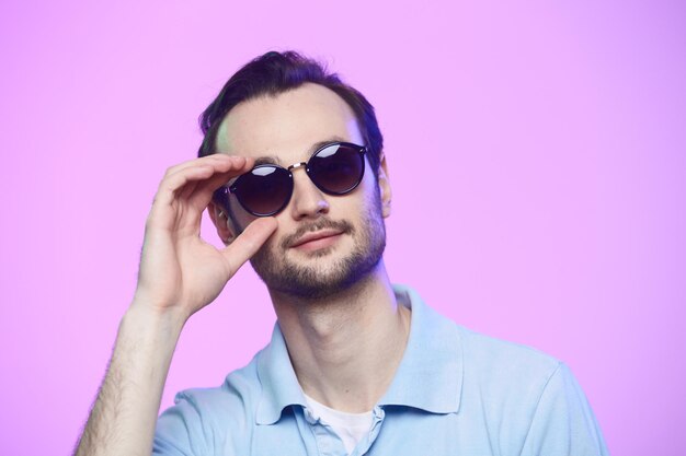 Foto de estúdio de homem bonito usando óculos escuros sobre fundo rosa