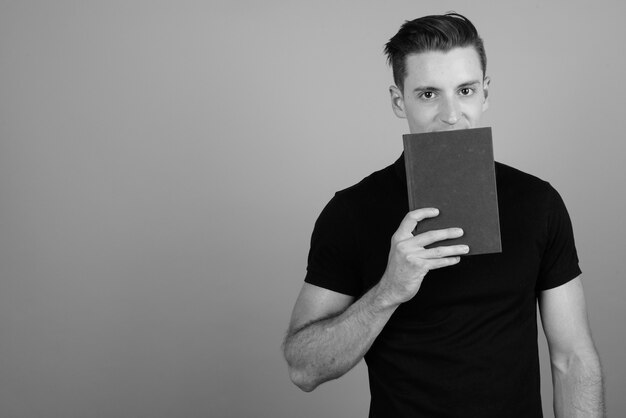 Foto de estúdio de jovem bonito lendo um livro contra um fundo cinza em preto e branco