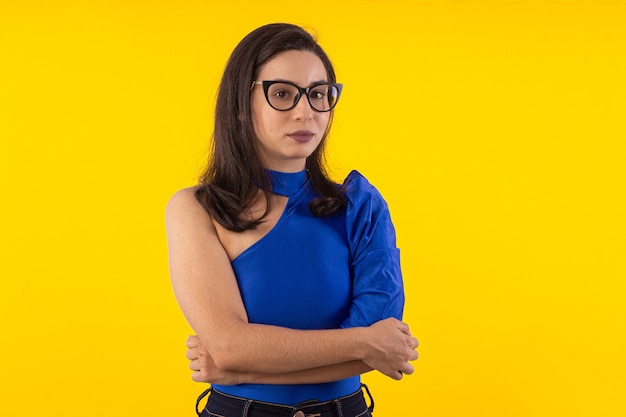 Foto de estúdio de jovem de óculos com blusa azul em fundo amarelo com expressão facial