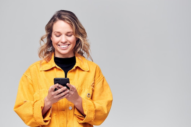 Foto de estúdio de jovem sorridente vestida casualmente usando telefone celular