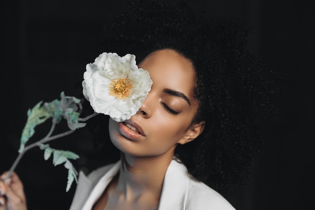 Foto de estúdio de modelo feminino de pele escura muito feliz ri alegremente e posa perto de flores