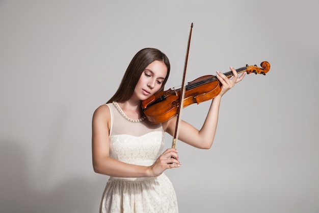 Foto de estúdio de morena de vestido branco toca violino.