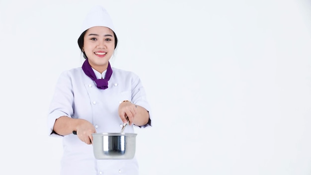 Foto de estúdio de retrato de restaurante profissional asiático cozinhando chef executivo feminino em uniforme de cozinheira e lenço em pé sorrindo olhar para a câmera segurando a panela de aço inoxidável e tampa em fundo branco.