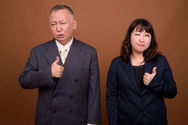 Foto de estúdio de um empresário japonês maduro e uma mulher de negócios japonesa madura juntos contra um fundo marrom