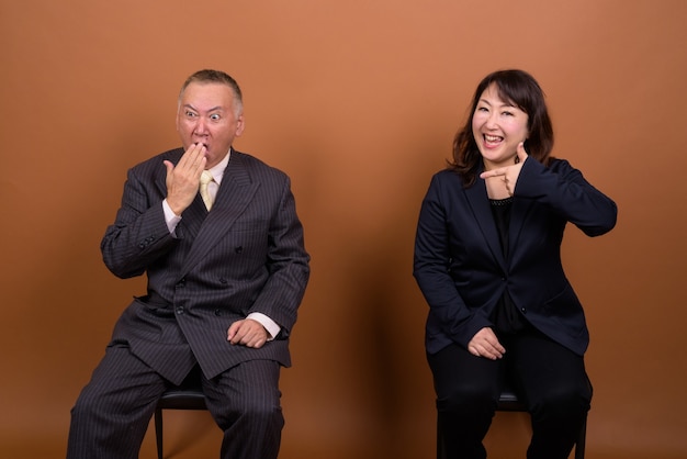 Foto de estúdio de um empresário japonês maduro e uma mulher de negócios japonesa madura juntos contra um fundo marrom