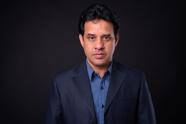Foto de estúdio de um homem de negócios indiano maduro bonito em um terno contra um fundo preto