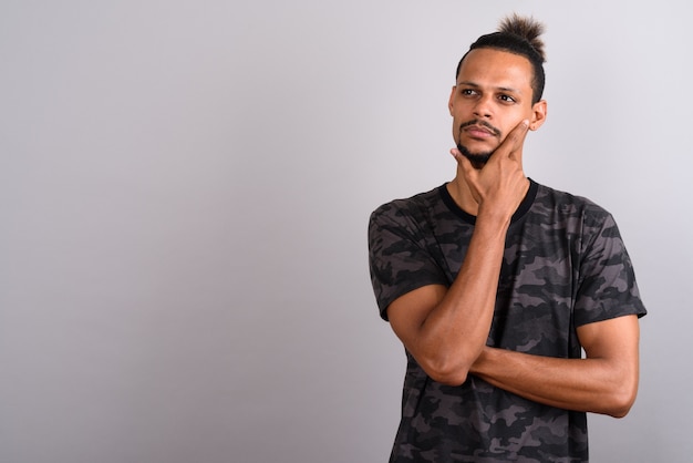 Foto foto de estúdio de um jovem africano bonito barbudo vestindo uma camisa com estampa de camuflagem e cabelo amarrado contra um fundo cinza