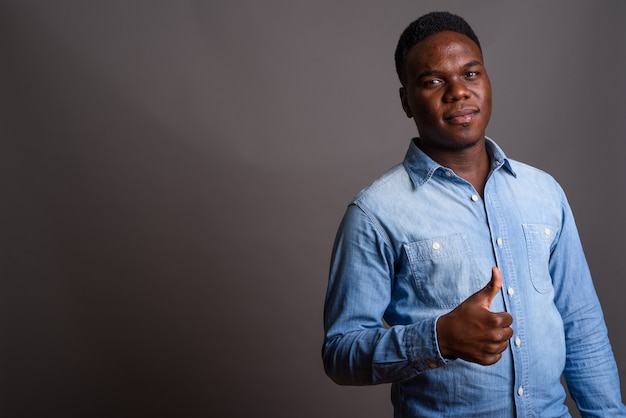 Foto de estúdio de um jovem africano vestindo uma camisa jeans contra um fundo cinza