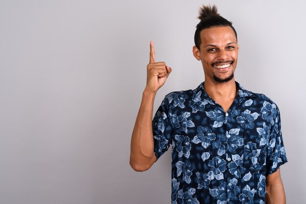 Foto de estúdio de um jovem bonito barbudo africano vestindo uma camisa havaiana com cabelo amarrado contra um fundo cinza