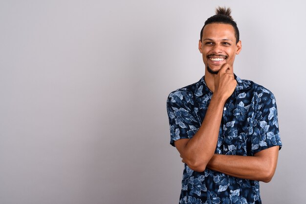 Foto de estúdio de um jovem bonito barbudo africano vestindo uma camisa havaiana com cabelo amarrado contra um fundo cinza