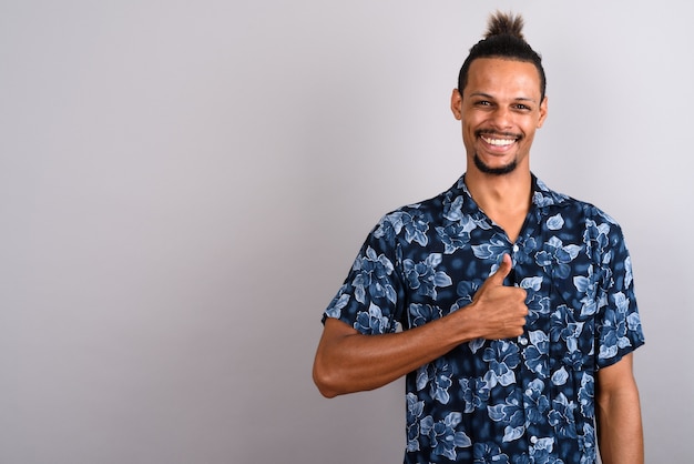 Foto de estúdio de um jovem bonito barbudo africano vestindo uma camisa havaiana com cabelo amarrado contra um fundo cinza