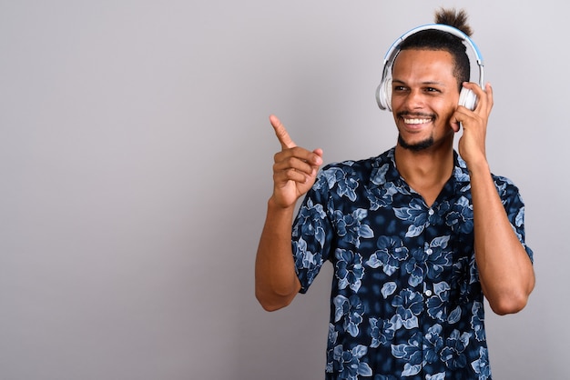 Foto foto de estúdio de um jovem bonito barbudo africano vestindo uma camisa havaiana enquanto ouve música contra um fundo cinza