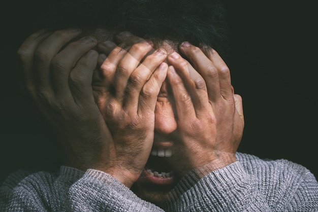 Foto de estúdio de um jovem experimentando angústia mental e gritando contra um fundo preto