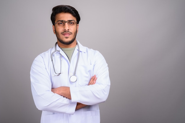 Foto de estúdio de um jovem indiano bonito médico contra o cinza