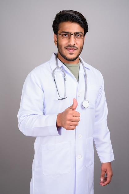 Foto de estúdio de um jovem indiano bonito médico contra o cinza