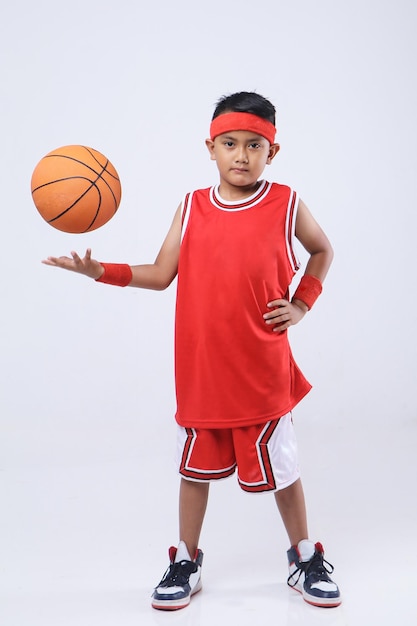 Foto de estúdio de um menino asiático em uma camisa vermelha segurando uma bola de basquete