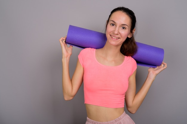 Foto de estúdio de uma bela jovem pronta para a academia sorrindo e parecendo feliz contra o cinza