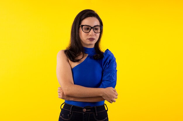 Foto de estúdio de uma jovem de óculos com blusa azul em fundo amarelo com várias expressões faciais